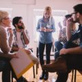 A group of people in a circle listening to a female speaking with a look of surprise on their faces