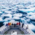 A group of people at the front of a ship as it breaks though ice