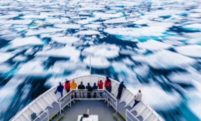 A group of people at the front of a ship as it breaks though ice