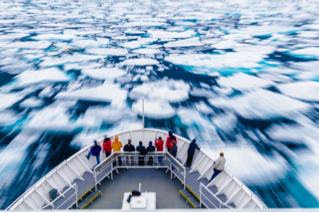 A group of people at the front of a ship as it breaks though ice